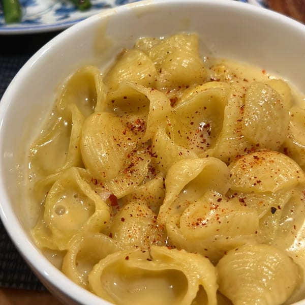 Close-up of creamy mac and cheese with shell pasta, topped with red pepper flakes in a white bowl.