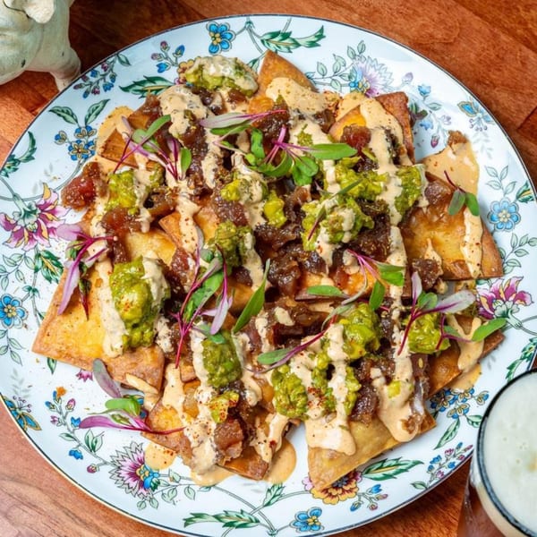 Harvey's nachos with guacamole, meat, and sauce on a floral plate next to a beer.