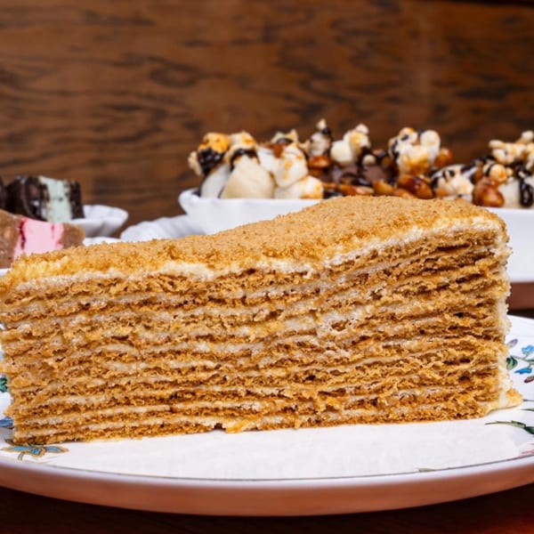 A large slice of multi-layered honey cake with a crumb topping on a decorative plate.