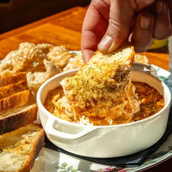 A hand dips a piece of toasted bread into a bowl of creamy, golden-brown dip at Harvey's.