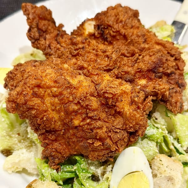 Crispy fried chicken pieces on a bed of fresh Caesar salad with croutons and a hard-boiled egg.
