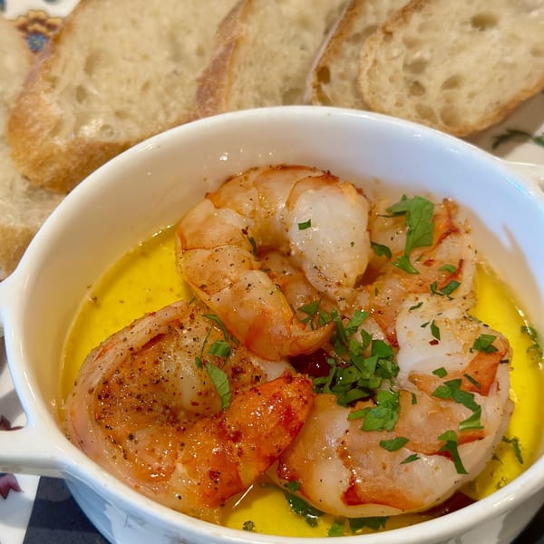 Shrimp scampi in a white bowl with garlic butter sauce and parsley, served with sliced bread.
