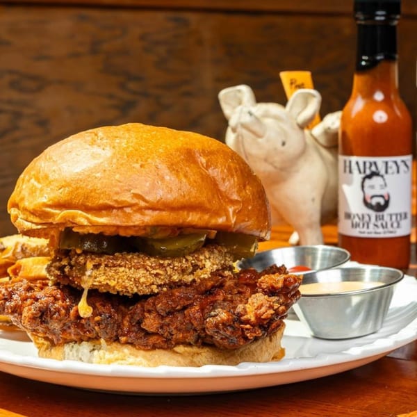 A Harvey's fried chicken sandwich with pickles, a side of fries, and hot sauce.