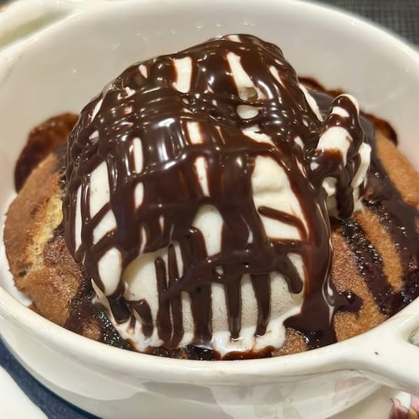 A warm chocolate chip cookie topped with vanilla ice cream and drizzled with chocolate sauce.